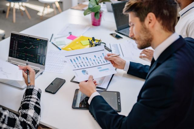 Technical-Expertise - Nwaresoft Private Limited - Nwaresoft Private Limited Team of professionals reviews financial charts and reports at a white table with laptops and tablets nearby.
