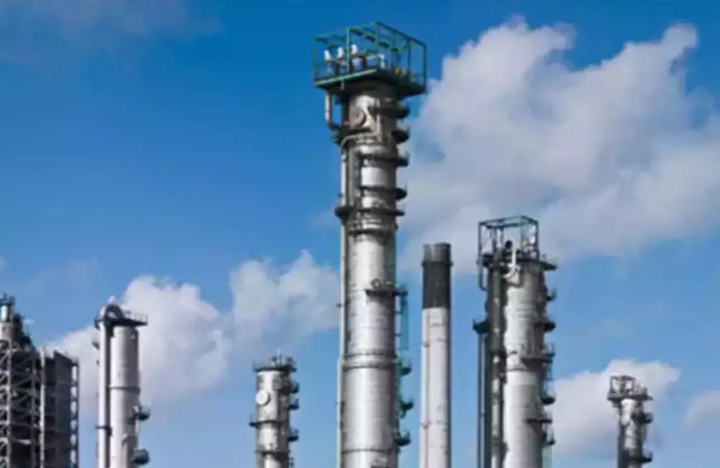 - - Tall industrial refinery towers and pipes set against a blue sky.