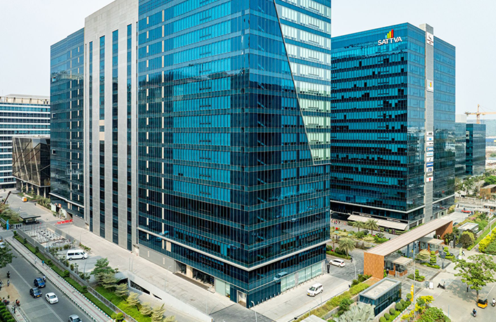 - - Aerial view of blue glass office towers in a modern business district, with streets, cars, and greenery at the base.
