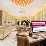 - Sales associate at a desk in a gold-toned jewelry store, looking at a computer displaying a colorful data dashboard.