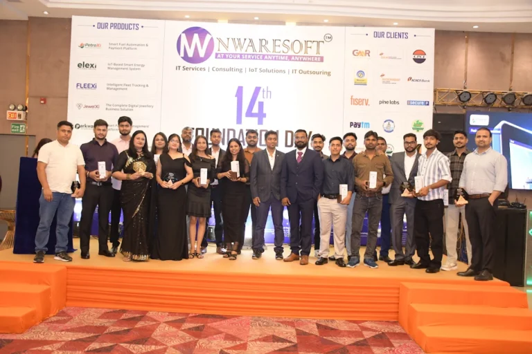 - Group of award recipients on a stage holding trophies during a company event, with a banner reading '14th Foundation Day' behind them.